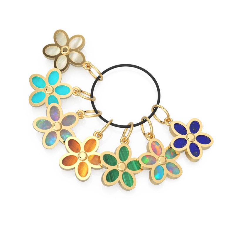 May include: A set of seven gold flower charms with different colored gemstones. The charms are attached to a black cord.