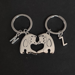 May include: Two silver keychains with cat-shaped charms that fit together to form a heart. The charms have the letters "N" and "Z" attached to them.