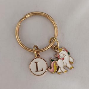 May include: Gold key ring with a white unicorn charm and a gold circle charm with the letter L on it.