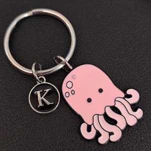 May include: Pink jellyfish keyring with a silver key ring and a black charm with the letter K.