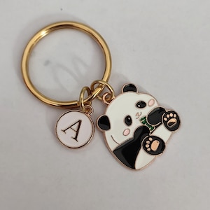 May include: Gold key chain with a white and black panda charm holding a green bamboo shoot and a small round charm with the letter A.