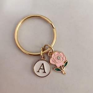 May include: Gold key chain with a pink flower charm and a white letter A charm. The flower charm has a small rhinestone in the center.