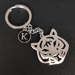 May include: Silver key chain with a black metal tiger charm and a black metal charm with the letter K.