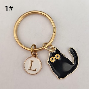 May include: Gold key chain with a black cat charm and a white circle charm with the letter L on it.