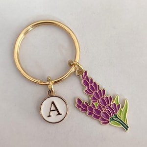 May include: Gold key chain with a purple flower charm and a white circle charm with the letter A.