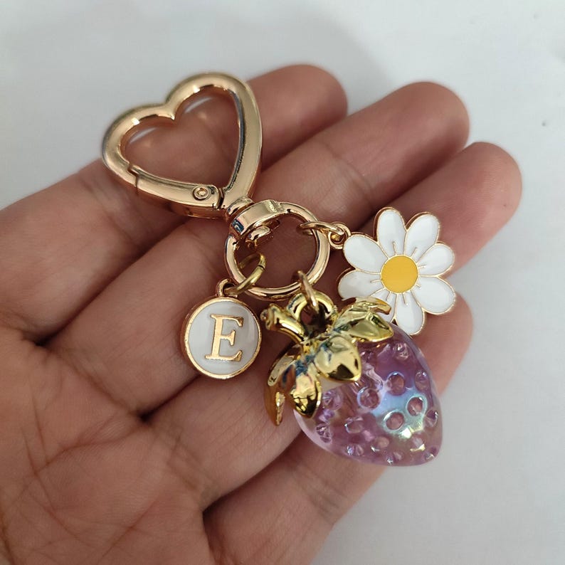 May include: Gold-tone keychain with a heart-shaped ring, a letter E charm, a pink strawberry charm, and a white daisy charm.