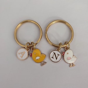 May include: Two gold keychains with yellow and white chick charms. The charms have a letter 'A' and 'N' on them.