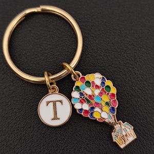 May include: Gold keyring with a white charm that says "T" and a colourful charm of a house with balloons.
