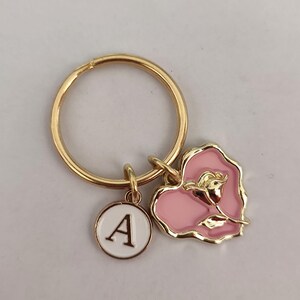 Könnte beinhalten: Goldener Schlüsselanhänger mit einem rosa Herz-Anhänger mit einer goldenen Rose und einem weißen Kreis-Anhänger mit dem Buchstaben A.