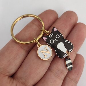 May include: Gold key chain with a black and white cat charm with pink ears and a white circle charm with the letter N in gold.