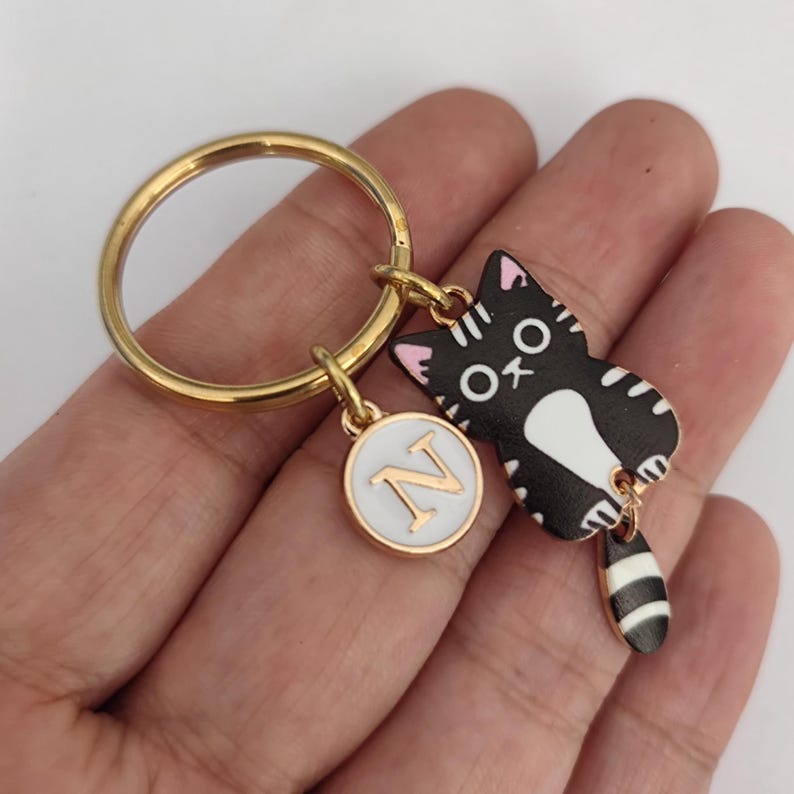 May include: Gold key chain with a black and white cat charm with pink ears and a white circle charm with the letter N in gold.
