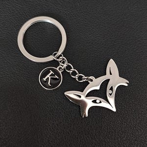 May include: Silver fox keychain with a silver key ring and a small round charm with the letter "K" in black on a silver background.