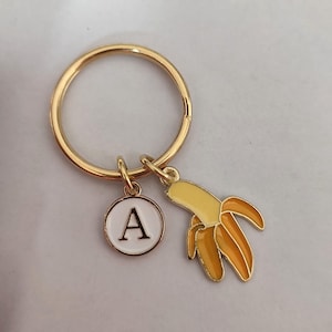 May include: A gold key chain with a white circle charm with the letter A and a yellow banana charm.
