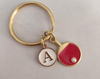 May include: Gold keychain with a red and white ping pong paddle charm and a white letter A charm.