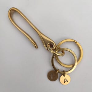 Könnte beinhalten: Ein goldfarbener Schlüsselanhänger mit einem Haken, zwei Ringen und zwei runden Anhängern mit den eingravierten Buchstaben "A" und "Z".
