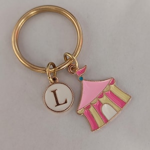 May include: Gold key ring with a pink and yellow striped tent charm and a white circle charm with the letter L in gold.