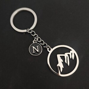 May include: Silver keyring with a mountain silhouette charm and a small round charm with the letter N.