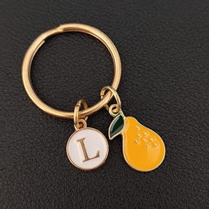 May include: Gold key ring with a white circle charm with the letter L and a yellow pear charm.