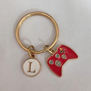 May include: Gold key ring with a red video game controller charm and a white circle charm with the letter L.