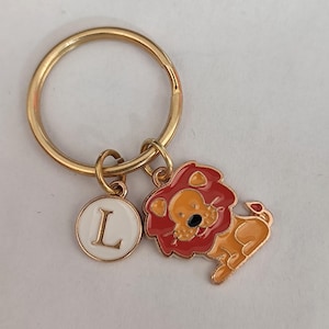 May include: Gold keychain with a lion charm and a round charm with the letter L in white on a gold background.