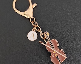 May include: A gold-colored keychain with a violin charm and a round charm with the letter "A". The violin is brown with gold accents and a bow. The keychain has a lobster clasp.