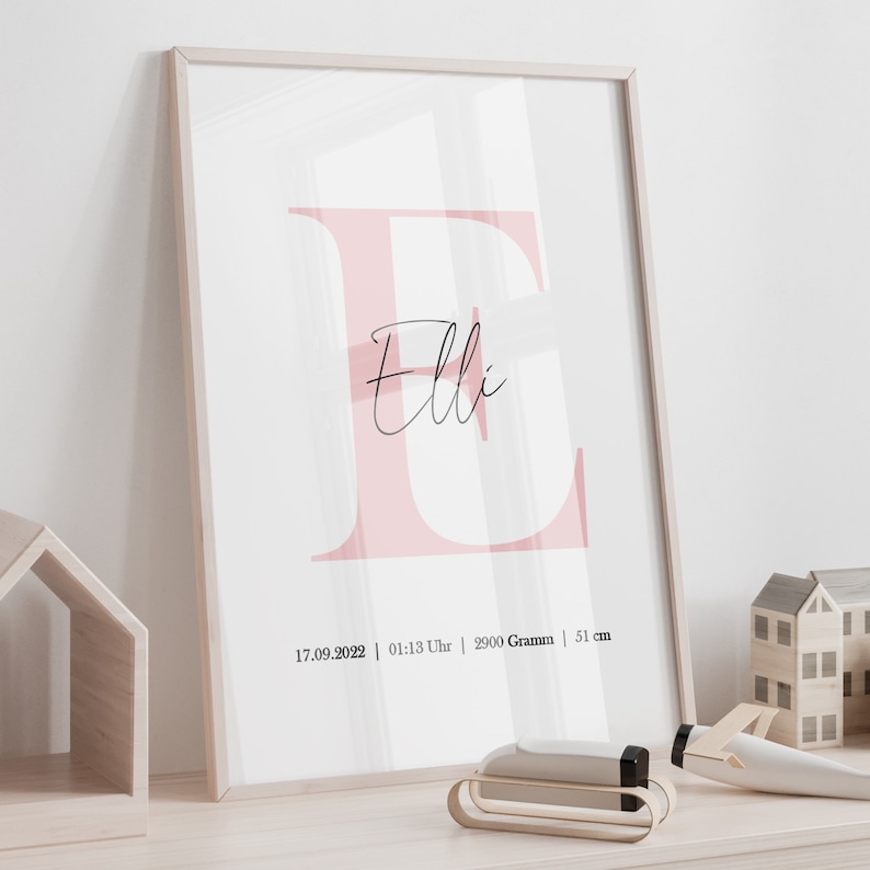 May include: A pink and white framed print with the letter "E" in pink and the name "Elli" written in cursive. The print also includes the date "17.09.2022", time "01:13 Uhr", weight "2900 Gramm", and length "51 cm".