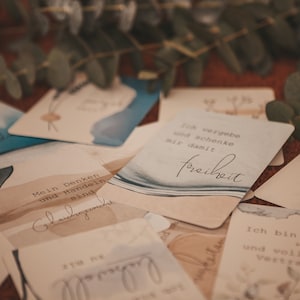 May include: A set of affirmation cards with watercolor backgrounds. The cards feature phrases in German, including "Mein Denken und Handeln sind" and "Ich vergebe und schenke mir damit Freiheit".