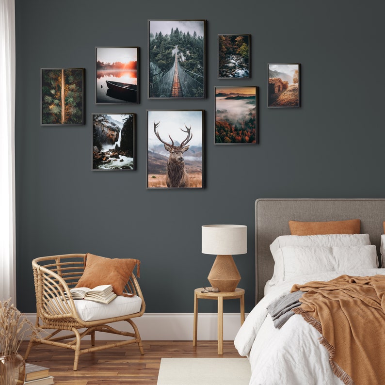May include: A bedroom interior with a gray wall, a white bed with a brown blanket, a brown wicker chair with a white cushion, a brown lamp on a wooden table, and a collection of framed nature photographs on the wall.
