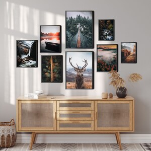 May include: A collection of eight framed nature photographs, including a deer, a bridge, a lake, a waterfall, and a forest. The photos are arranged in a grid pattern on a light gray wall above a wooden cabinet with a woven rattan front.