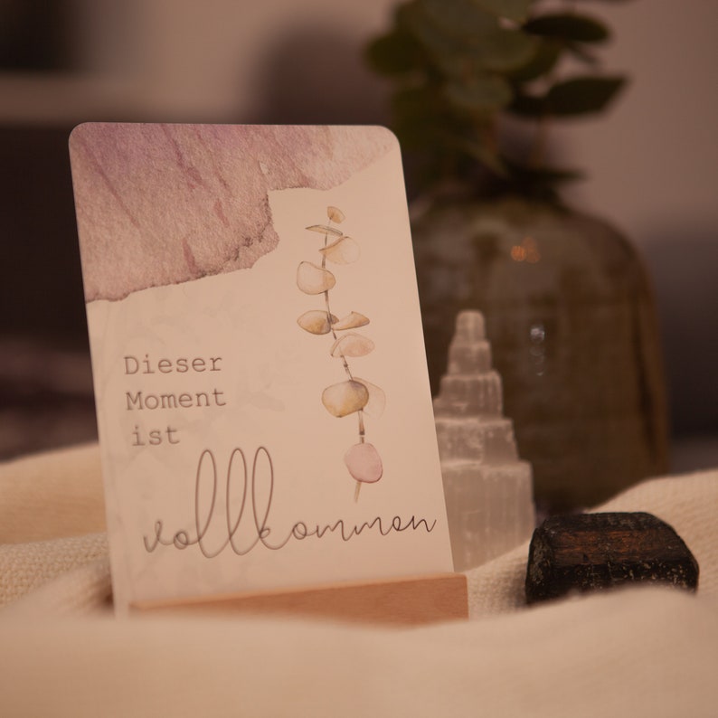 May include: A light brown card with a watercolor design of a eucalyptus branch. The card reads "Dieser Moment ist vollkommen" which translates to "This moment is perfect".
