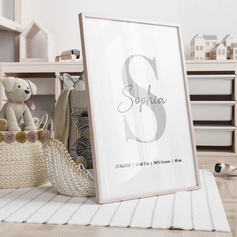 May include: A framed print with a large gray letter "S" and the name "Sophia" written in cursive below. The print also includes the date "17.04.2023", time "01:45 Uhr", weight "3070 Gramm", and length "49 cm".