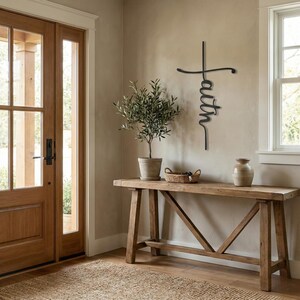 a wooden console table with a vase and a basket on top, situated in a room with a large window and a cross-shaped sign on the wall.