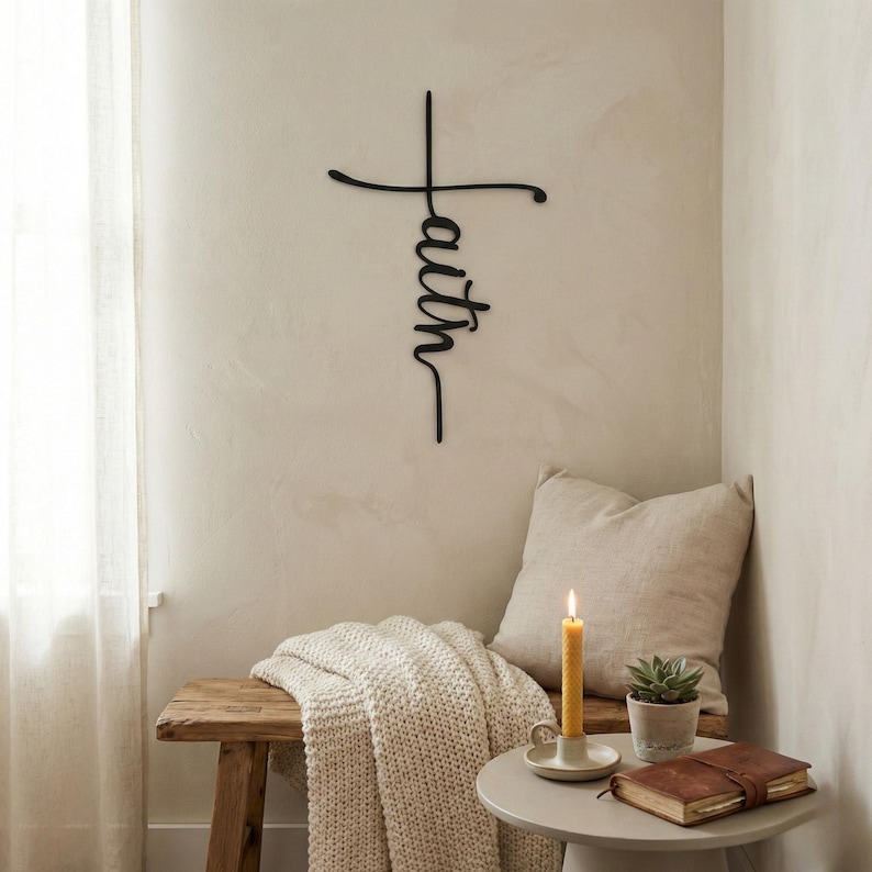 a cozy corner of a room with a wooden bench, a white pillow, a candle, and a small table with a book and a plant. The wall behind these items has a large black cross-shaped sign with the word "Faith" written on it.