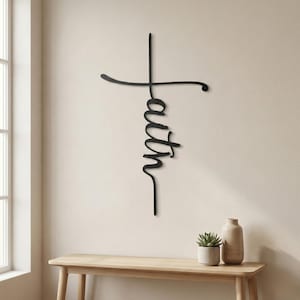a wooden table with a vase and a potted plant on it, set against a light-colored wall with a large black cross-shaped sign hanging above it.