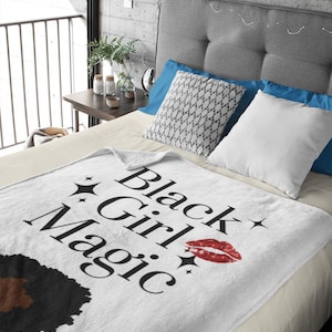 May include: White throw blanket with the text "Black Girl Magic" in black script, a red lipstick kiss mark, and black star accents. The blanket features a black and brown afro graphic.