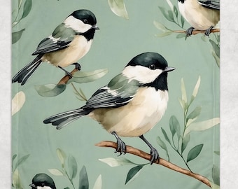 May include: A soft, light green blanket featuring an all-over pattern of watercolor-style birds perched on branches with green leaves. The birds have black and white heads, gray wings, and tan bodies. The blanket is a cozy home decor item.