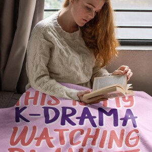 May include: A pink fleece blanket with the text "This is my K-Drama watching blanket" in purple, pink, and orange lettering.