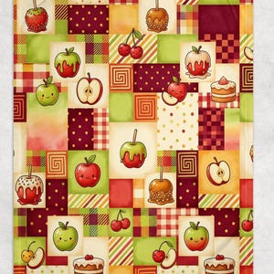 May include: A rectangular fleece blanket featuring a patchwork pattern of squares in shades of red, green, and cream. The design includes illustrations of whole apples, sliced apples, caramel apples, cherries, and small cakes with a cartoon aesthetic.