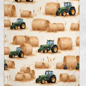 May include: A blanket with a repeating pattern of green tractors and hay bales on a cream background. The tractors have yellow wheels and are interspersed with brown hay bales and wheat stalks. The design has a rural, farm theme.