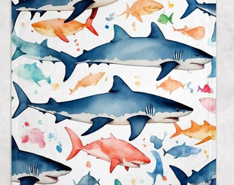 May include: A white blanket featuring a watercolor pattern of various sharks in shades of blue, orange, pink, and green. The design includes large sharks and smaller fish, with colorful paint splatters scattered across the surface.