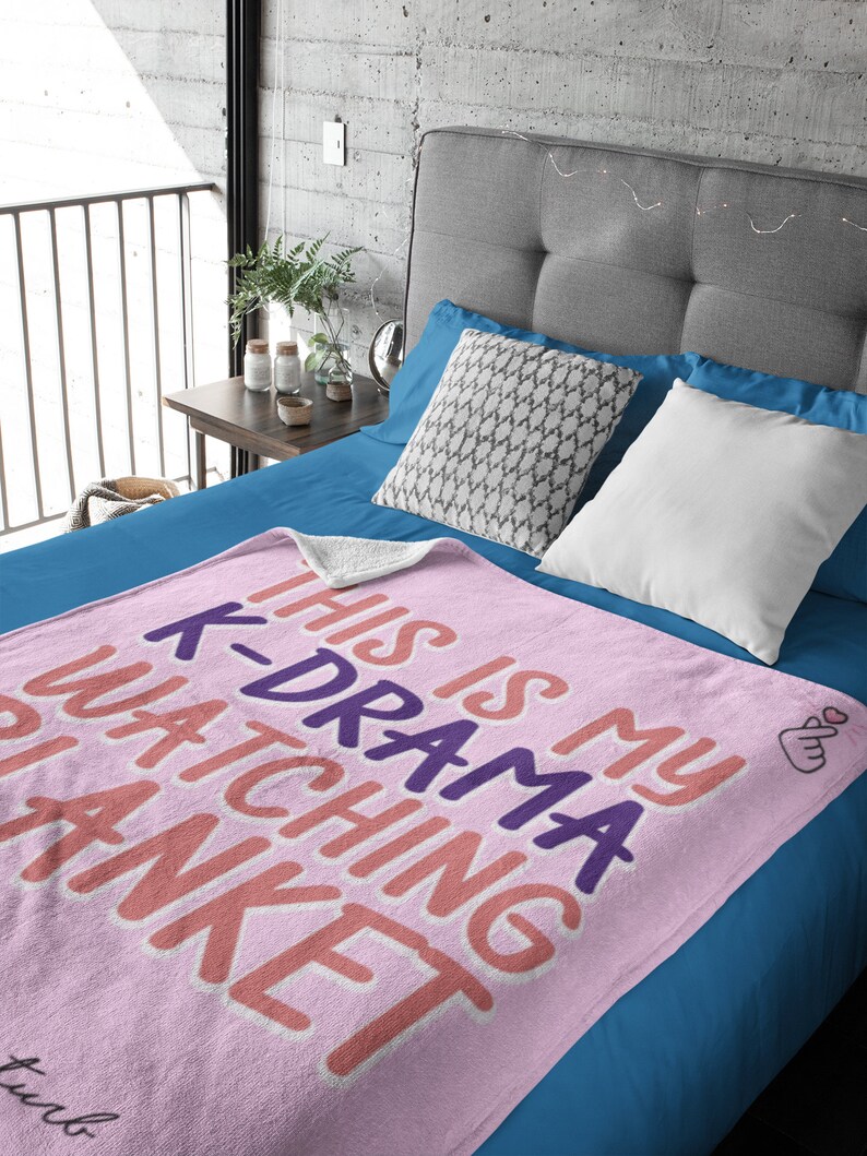 May include: Pink fleece blanket with the text "This is my K-Drama watching blanket" in pink, orange, and purple. The blanket has a small pink heart hand gesture in the corner.