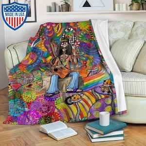 Peut inclure: Une couverture en molleton psychédélique colorée représentant un personnage de dessin animé hippie jouant de la guitare et assis sur une souche d'arbre. L'arrière-plan est rempli de motifs tourbillonnants, de champignons et d'un arc-en-ciel.