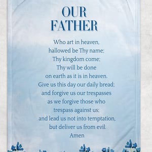 May include: A light blue blanket with the text "OUR FATHER" at the top. The text of the Lord's Prayer is printed below in a dark blue font. Blue floral accents are at the bottom.