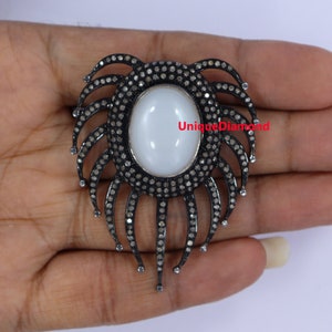 May include: A silver pendant with a white oval gemstone surrounded by a halo of black diamonds. The pendant features a design of black diamond-encrusted spikes radiating outwards.