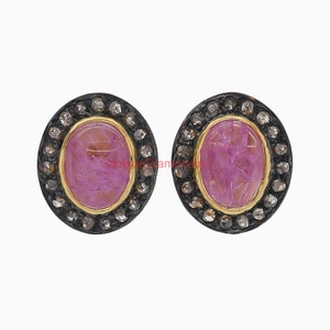 May include: A pair of oval-shaped earrings with a pink gemstone centre surrounded by a halo of small diamonds. The earrings have a black oxidised silver setting.