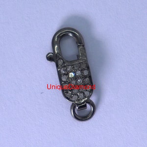 May include: A silver-toned clasp with a small, round ring at the bottom. The clasp is covered in tiny, clear diamonds.