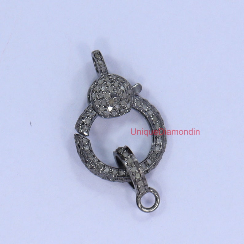 May include: Silver tone clasp with a round design, encrusted with small white diamonds.  The clasp is open and ready to be attached to a necklace or bracelet.
