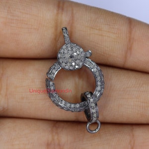 May include: A silver-toned clasp with a round, pave-set diamond design. The clasp is made of metal and has a polished finish.