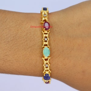 Peut inclure: Bracelet en or orné de pierres précieuses. Il présente un motif répété de pierres rouges, vertes et bleues de forme ovale, entrecoupées de petits diamants. Le bracelet mesure environ 17,78 cm de long.
