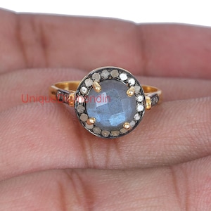 May include: A silver ring with a round, blue labradorite gemstone surrounded by a halo of small, white diamonds. The ring is set in gold.